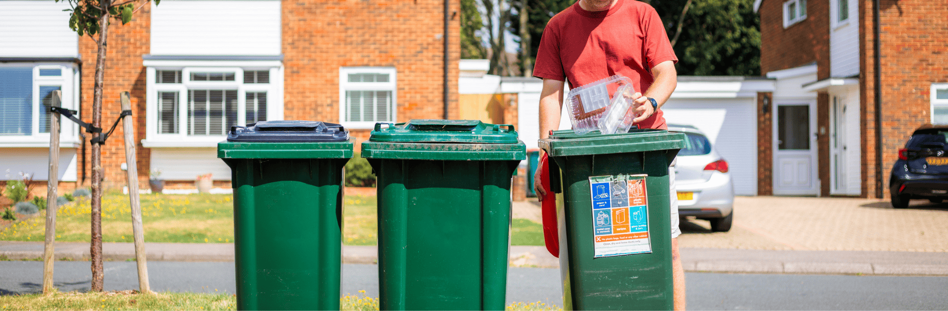 A resident putting an item into a green kerbside recycling bin