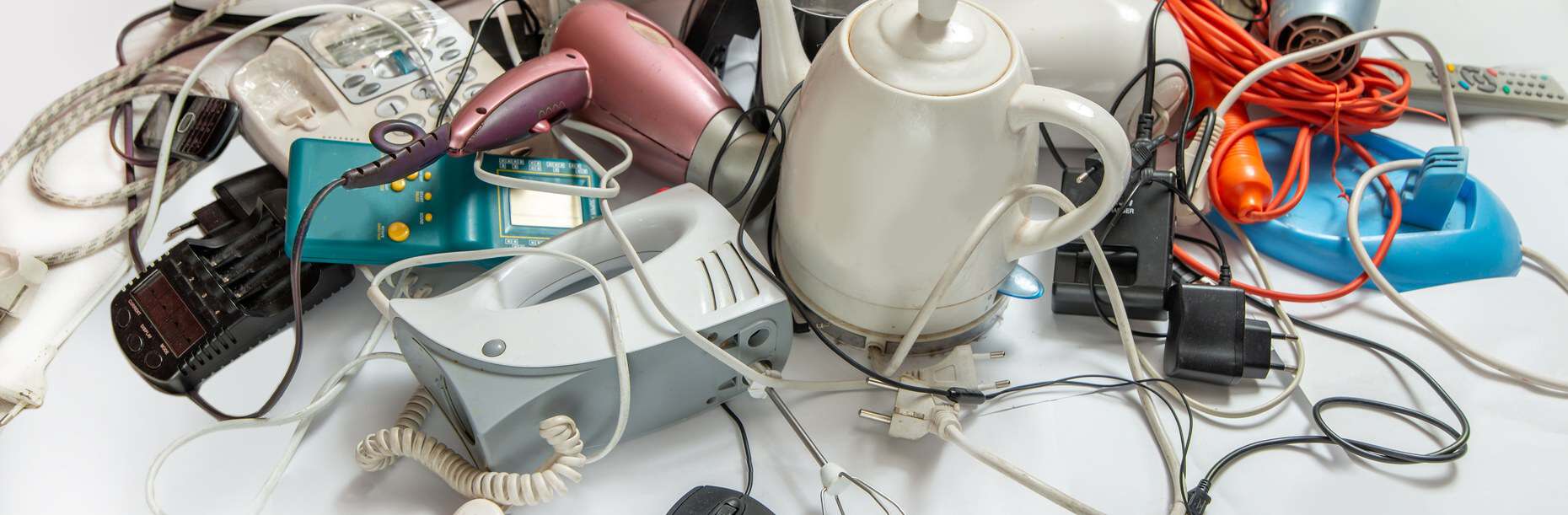 A pile of old electrical items including a kettle, hairdryer, phones and cables