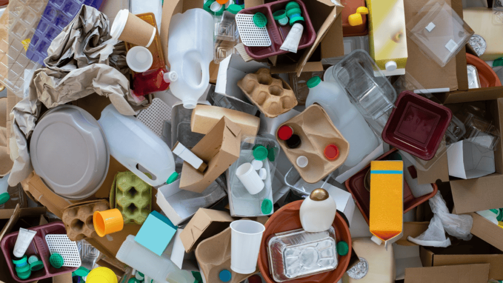 Pile of mixed recycling and rubbish. Including plastic bottles, cardboard boxes and trays, plastic trays, lids and takeaway coffee cups.