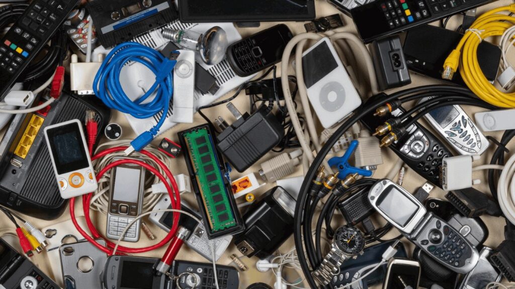 A messy pile of electronics including old phones, ipods, tv remotes and colourful wires